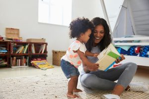 A Black young mother sitting on the floor teaching her young child to read in a bright room