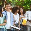 Group of diverse high school seniors outdoors in front of green treeline talking into each other lined up
