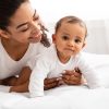 Young Black mother with an infant child all dressed in white playing on a white mattress.