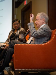 David Steiner sitting in a chair, holding a microphone, and speaking at a conference.