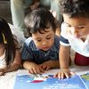 Three toddlers looking at a children's book.