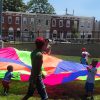 A group of children holding a colorful sheet outside.