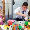 An adult helping young children at a craft table.