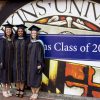 Three graduates posing for a photo under the Johns Hopkins University seal and "Class of 2019."