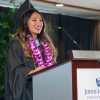 Stephanie Liu speaking at a podium wearing graduation regalia.