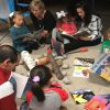 Several adults and young children reading books on the floor.