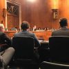 Several people in suits sitting and facing members of the Senate.