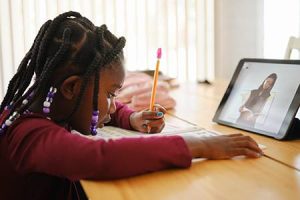 A child using a pencil while watching a video on a tablet.