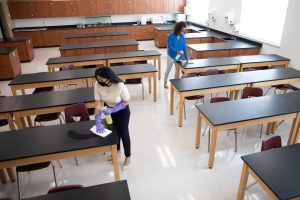 Adults in masks cleaning an empty classroom.