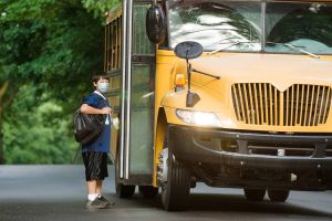 A child in a mask boarding a school bus.