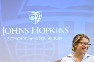 A person smiling in front of a Johns Hopkins School of Education sign.