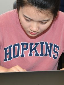 A person in a Hopkins t-shirt on a laptop.