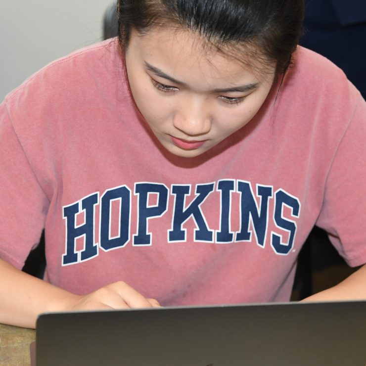 A person in a Hopkins t-shirt on a laptop.