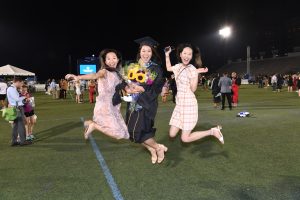 A graduate jumping happily with two people.