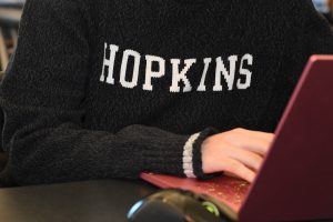 A person wearing a "Hopkins" sweater and typing on a laptop.