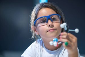 A child wearing goggles and playing with a toy molecule.