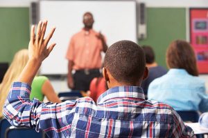 A teenager raising their hand in a classroom.