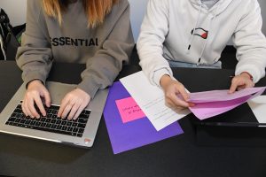 Two people in a classroom working on a laptop and looking at papers.