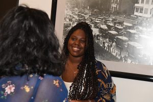 A person smiling and standing in front of a black and white photograph.