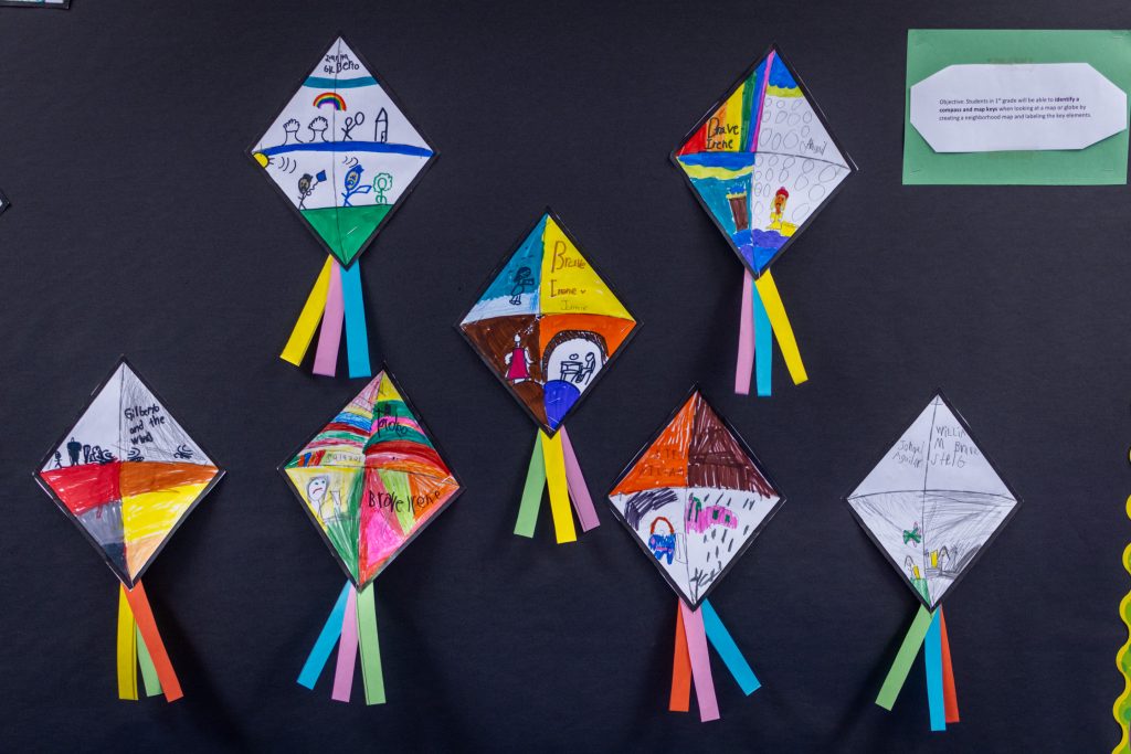 Children's small kites colored in and taped to a wall.