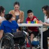 Group of special students in classroom, a down syndrome girl, two handicapped boys and Asian teacher playing toy and game together.