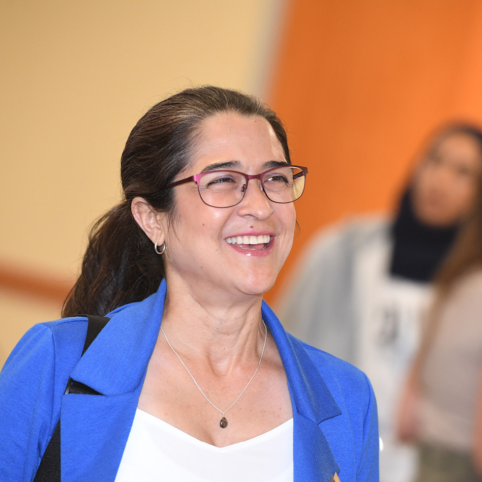 A woman wearing glasses, smiling and looking off into the distance.