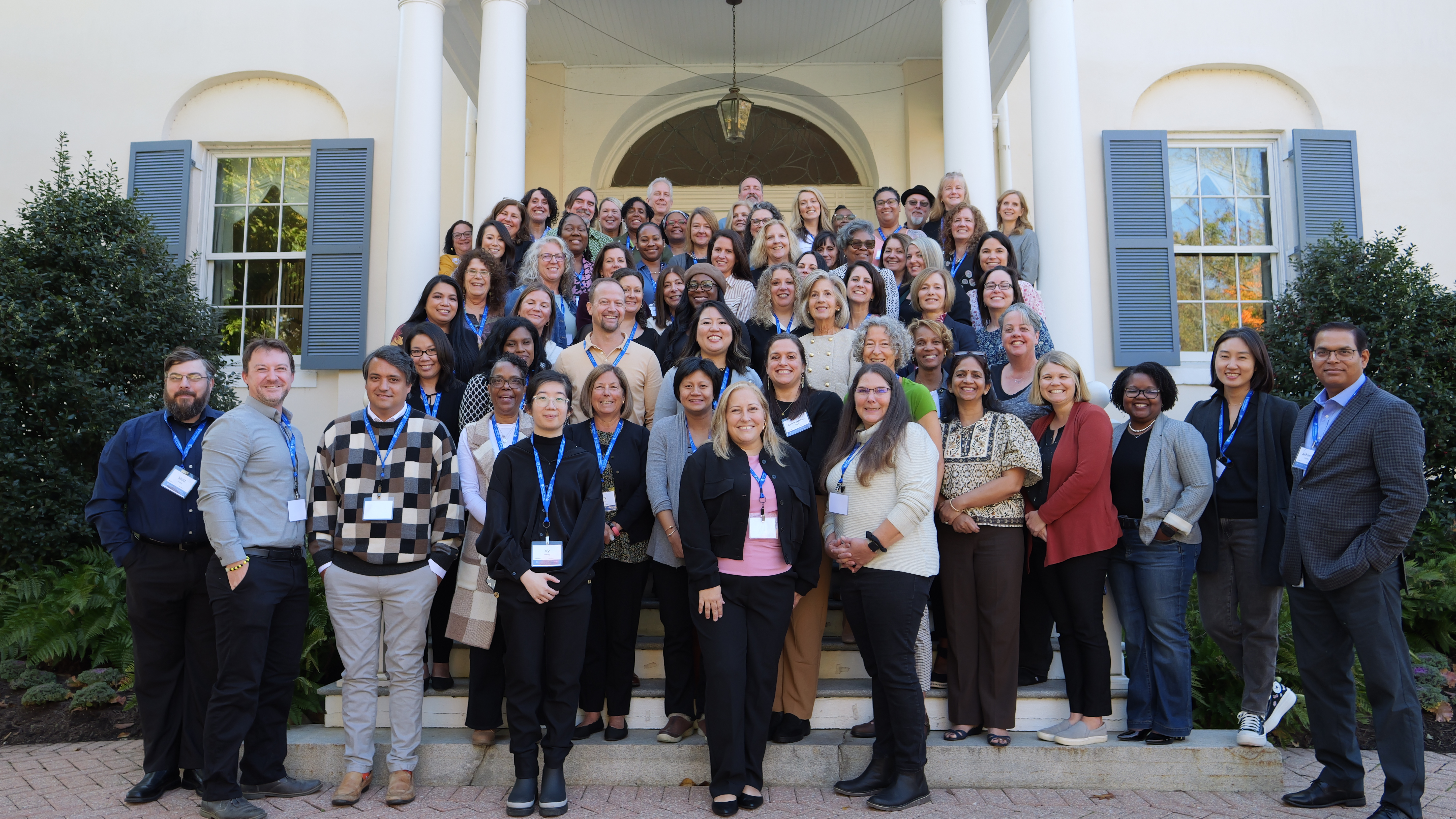 Group of professionals posing for a photo on steps in front of a building with white columns and blue shutters.