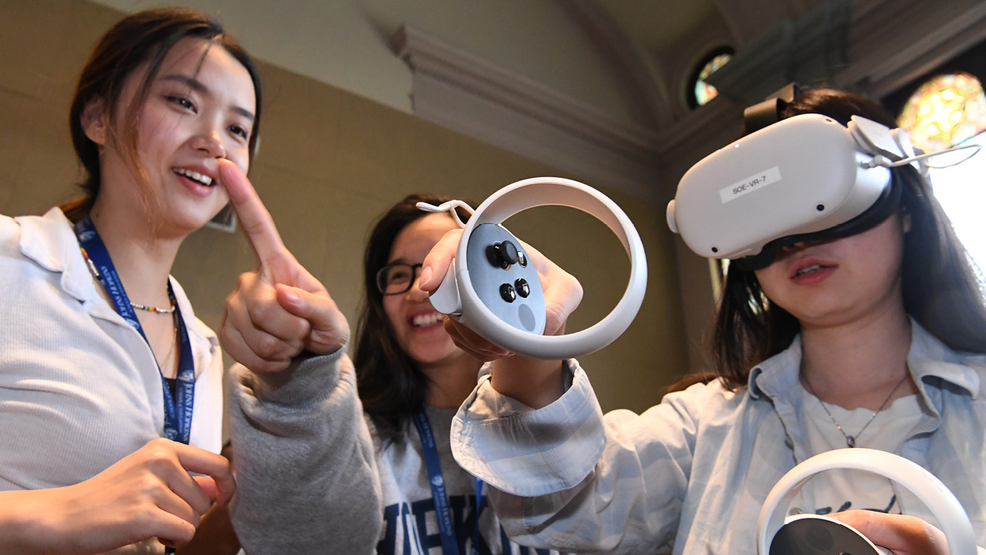 Three people engaging with a virtual reality headset.