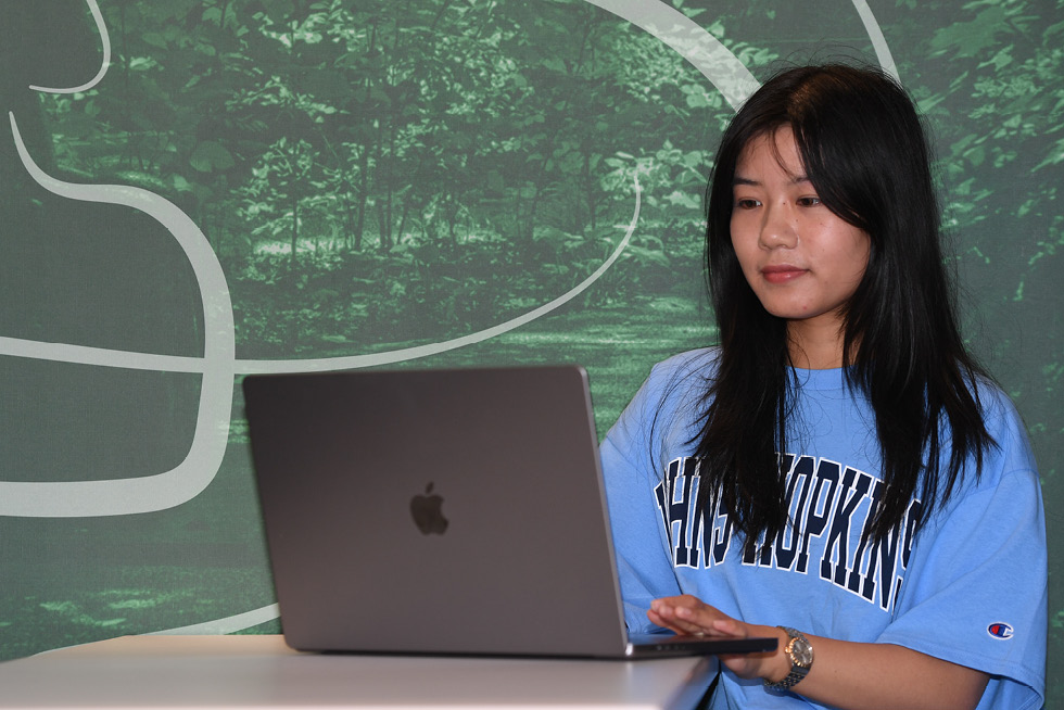 A person sitting at a laptop computer wearing a Johns Hopkins shirt.