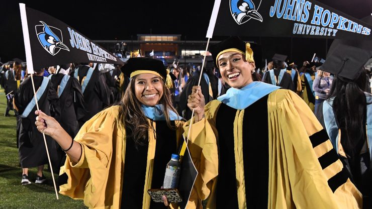 Two doctoral Graduates wave Johns Hopkins Pennants after Graduation