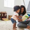 A Black young mother sitting on the floor teaching her young child to read in a bright room