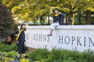 Two people near the marble wall on Johns Hopkins' Homewood campus