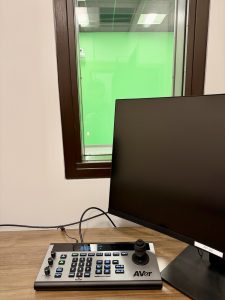 A computer monitor sitting on a table in a media observation room with a green screen in the background