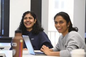 Two people sitting down, smiling at a table working on a laptop.
