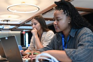 Two people sitting next to each other working on laptop computers