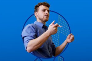 A person standing in front of a class holding a marker for a whiteboard with shapes in the background