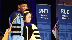 Professor Odis Johnson and newly hooded student pose for a photo on stage at the 2026 Doctoral Hooding event